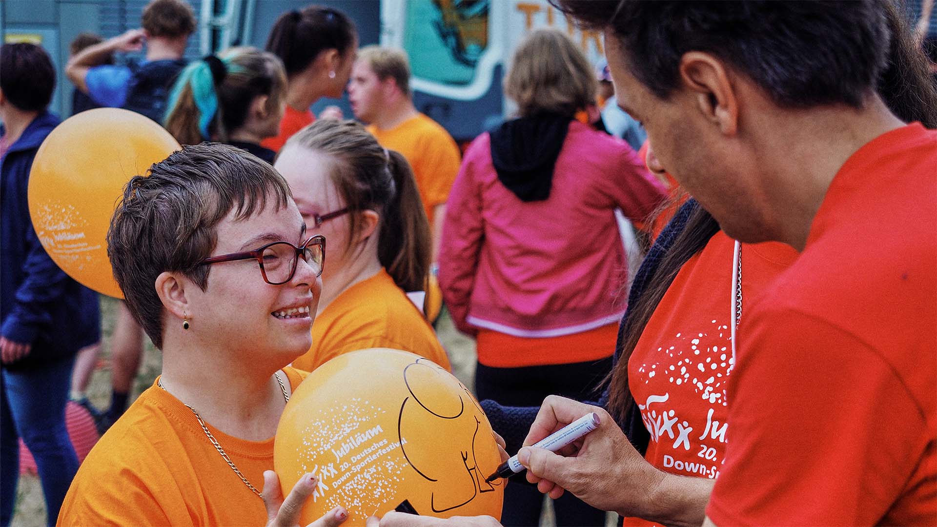 Foto: Moderator André Gatzke unterschreibt auf einem Ballon, den eine lachende Teilnehmerin hält.