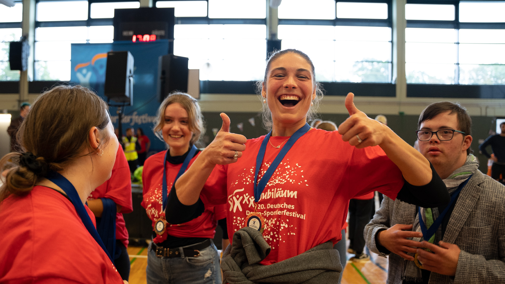 Foto: Lächelnde Frau mit Medaille hält beide Daumen hoch.