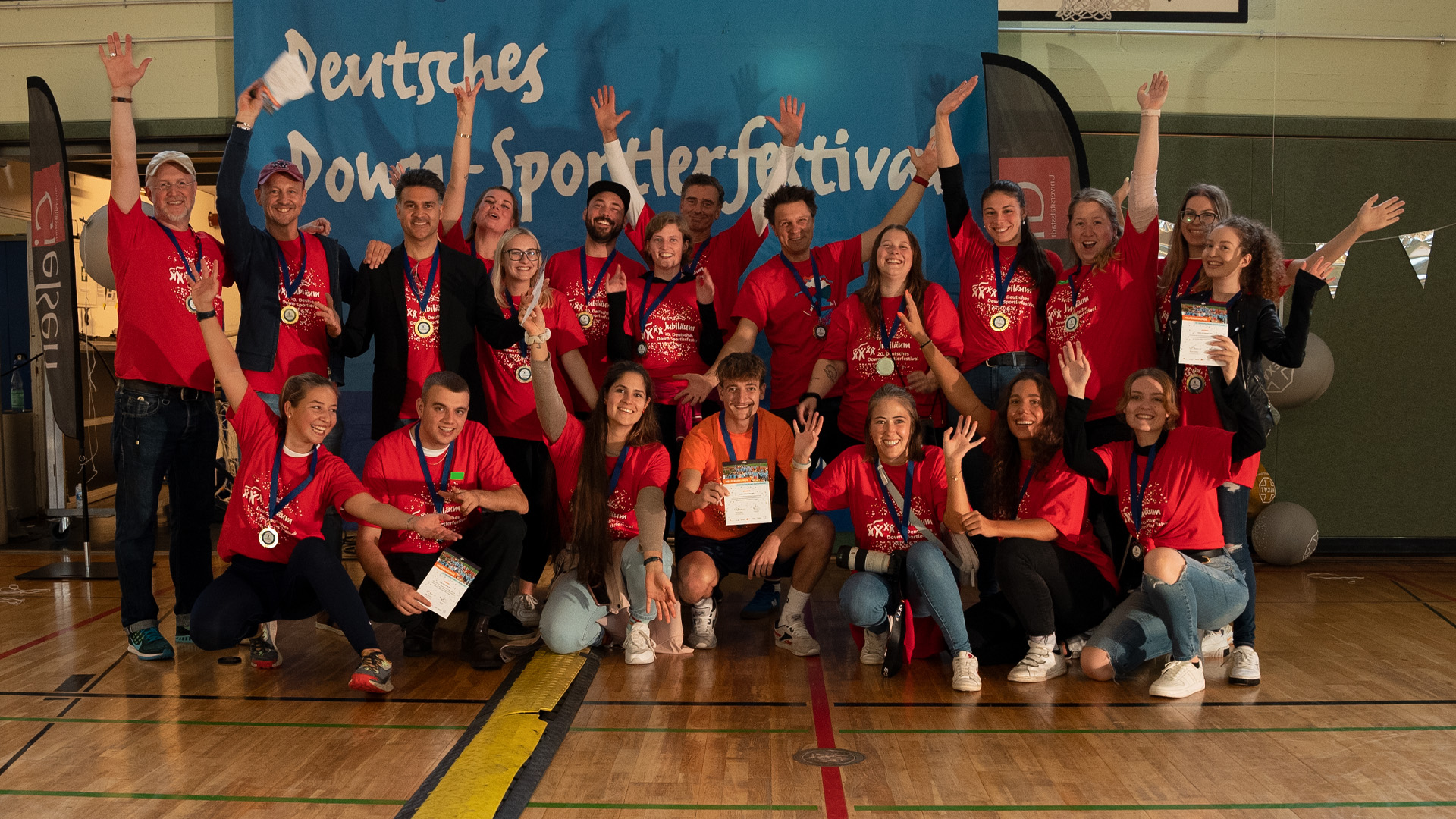 Foto: Große Gruppe von Helfenden jubelt vor dem Festivalbanner in der Halle.