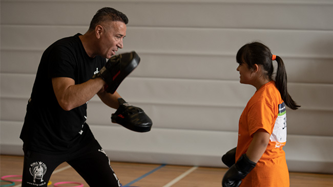 Foto: Coach hält Pratzen, während eine junge Teilnehmerin bereit zum Boxen ist.