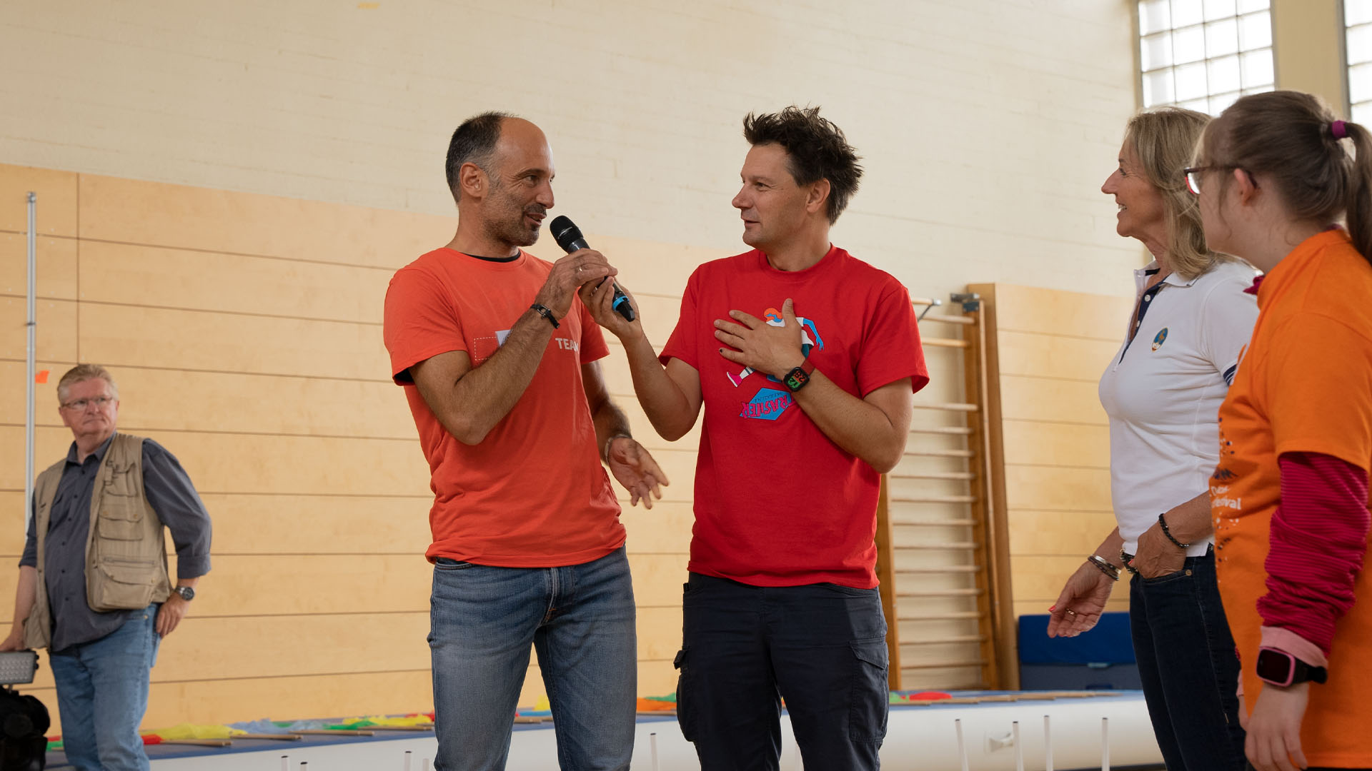 Foto: Moderator André Gatzke interviewt einen Mann in einer Sporthalle.