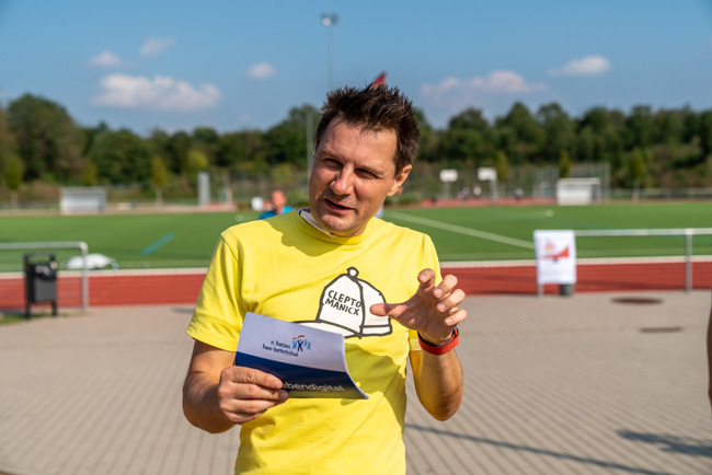 Foto: Moderator André Gatzke gestikuliert während einer Ansprache im Freien.