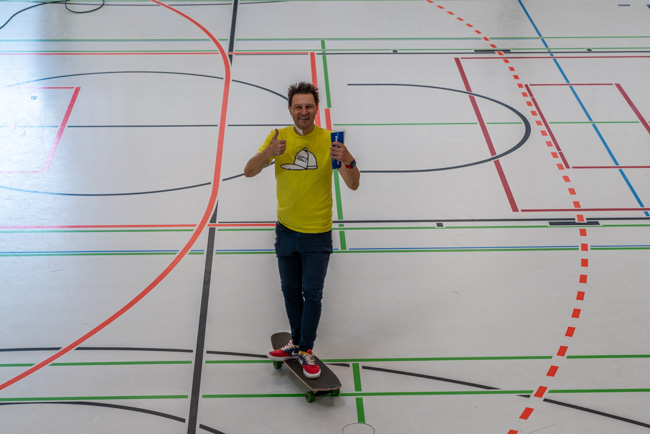 Foto: Moderator André Gatzke auf Skateboard in der Halle hält beide Daumen hoch.