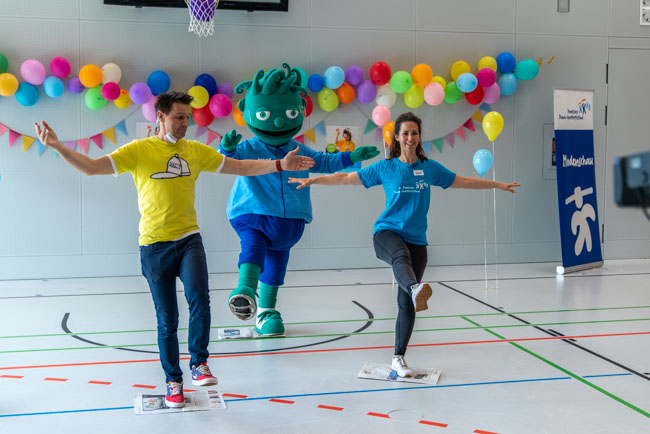 Foto: Moderator André Gatzke führt mit Frau und Maskottchen Balanceübungen aus.