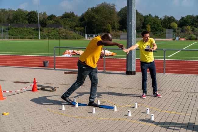Foto: Trainer zeigt eine Geschicklichkeitsübung mit Hindernissen auf dem Sportplatz.