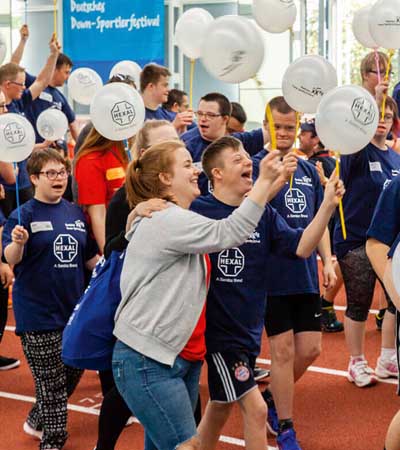 Foto: Zwei lachende Teilnehmende im blauen Shirt halten Ballons und jubeln.