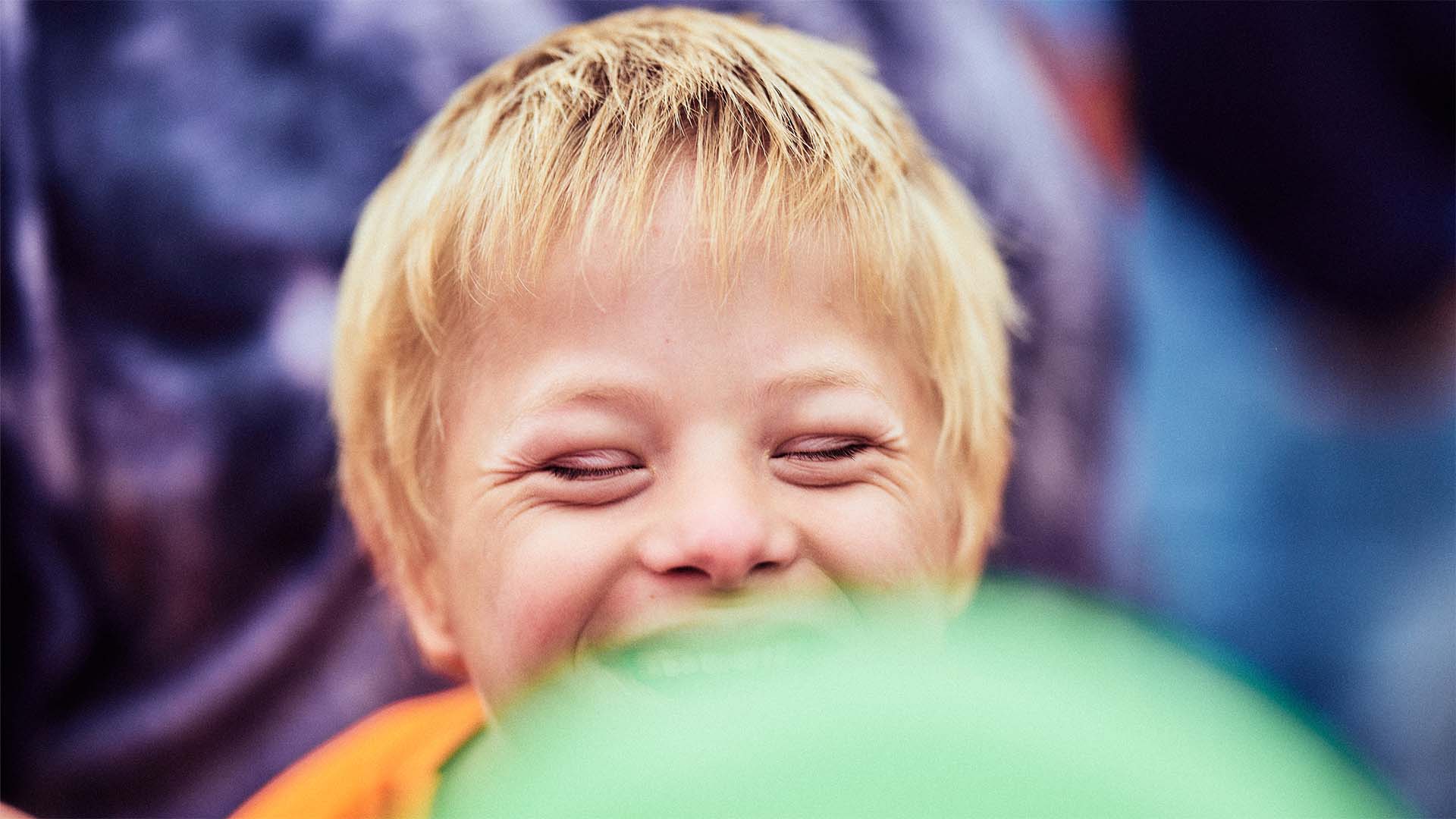 Foto: Nahaufnahme eines Jungen mit geschlossenen Augen, der herzlich lacht.
