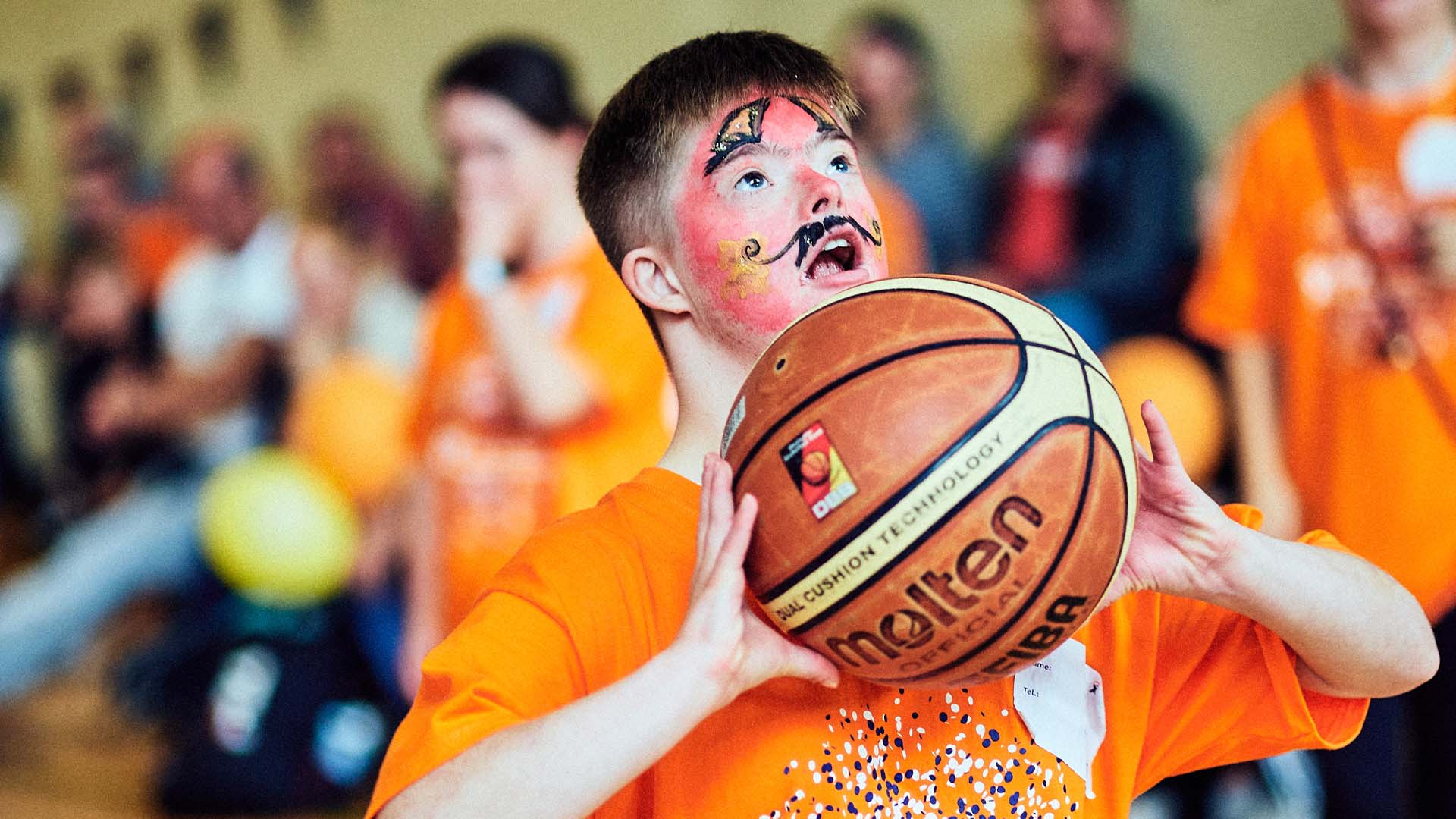 Foto: Junge mit Kinderschminke im Gesicht setzt mit Basketball zum Wurf an.