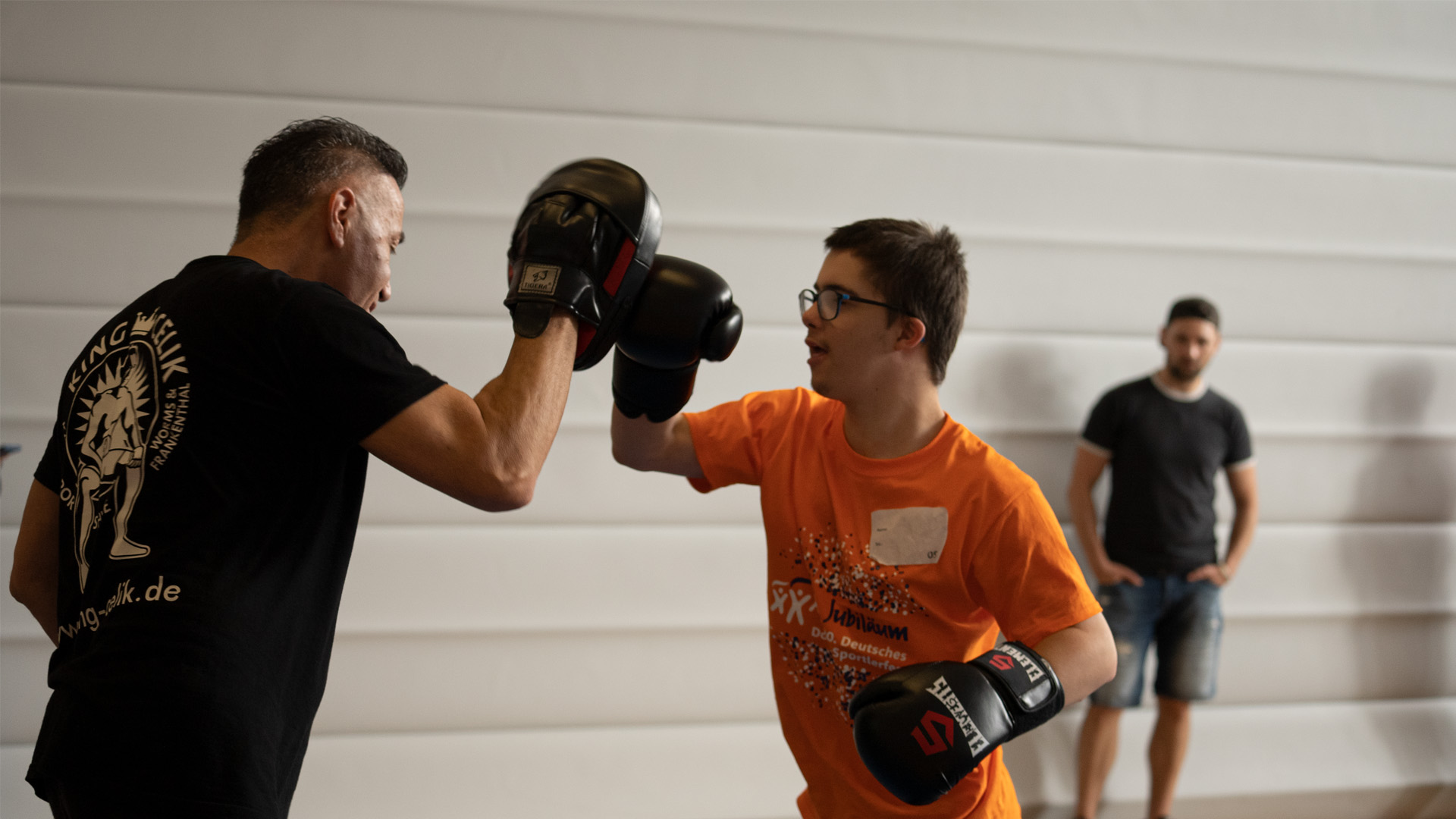 Foto: Teilnehmer im orangenen Shirt schlägt mit Boxhandschuh auf das Schlagpolster des Trainers.