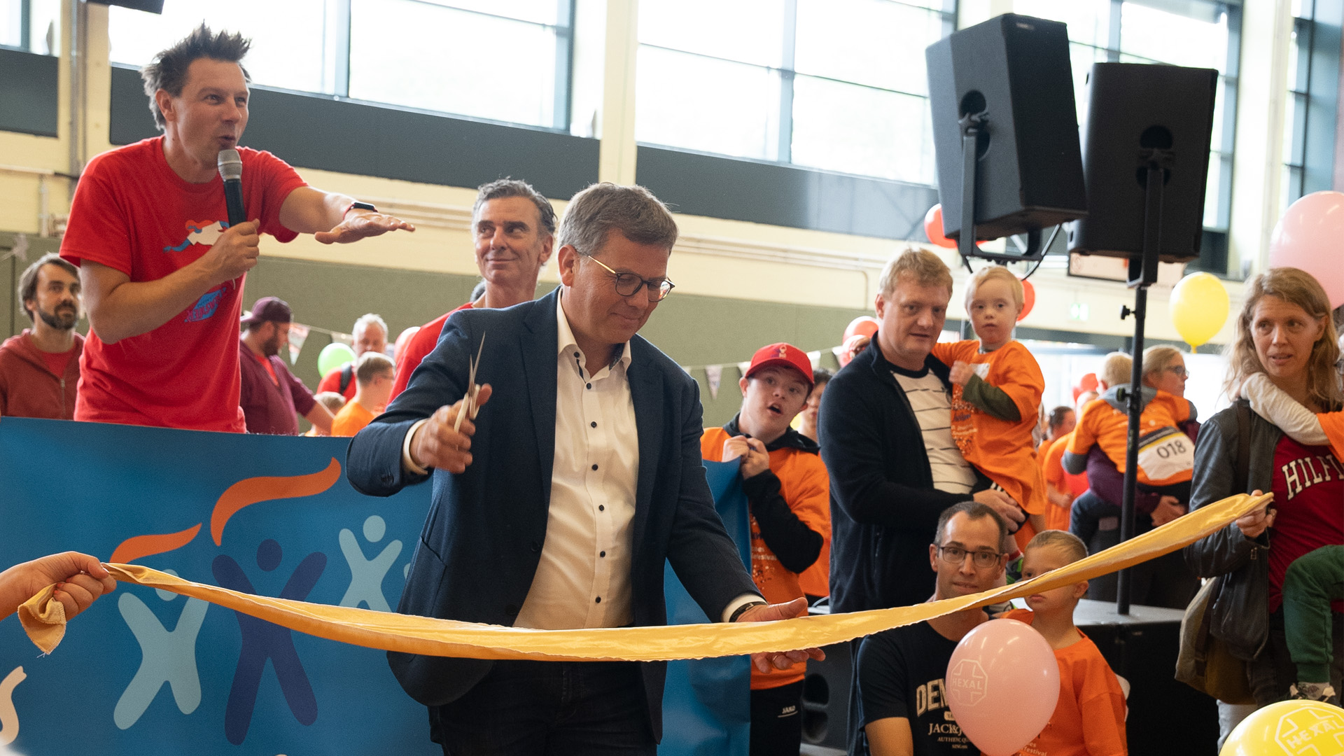 Foto: Mann im Anzug durchtrennt feierlich das orangefarbene Band zur Eröffnung der Veranstaltung.