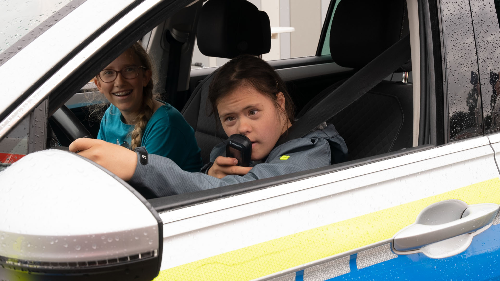 Foto: Mädchen im Auto hält ein Funkgerät an den Mund, Begleiterin lacht.